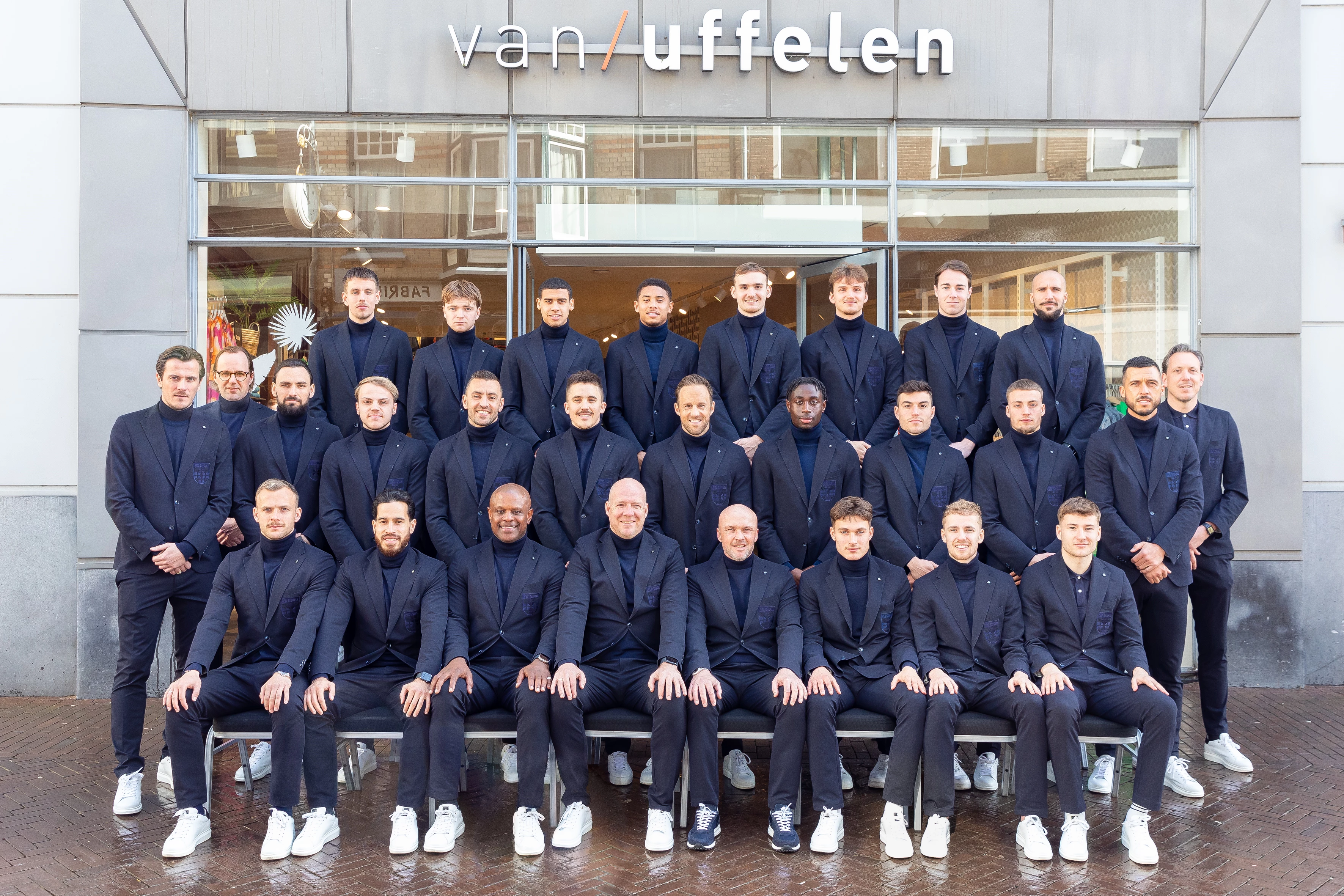 Voetbalteam PEC Zwolle poserend in pakken van Garl Gross voor de gevel van Van Uffelen Mode Zwolle